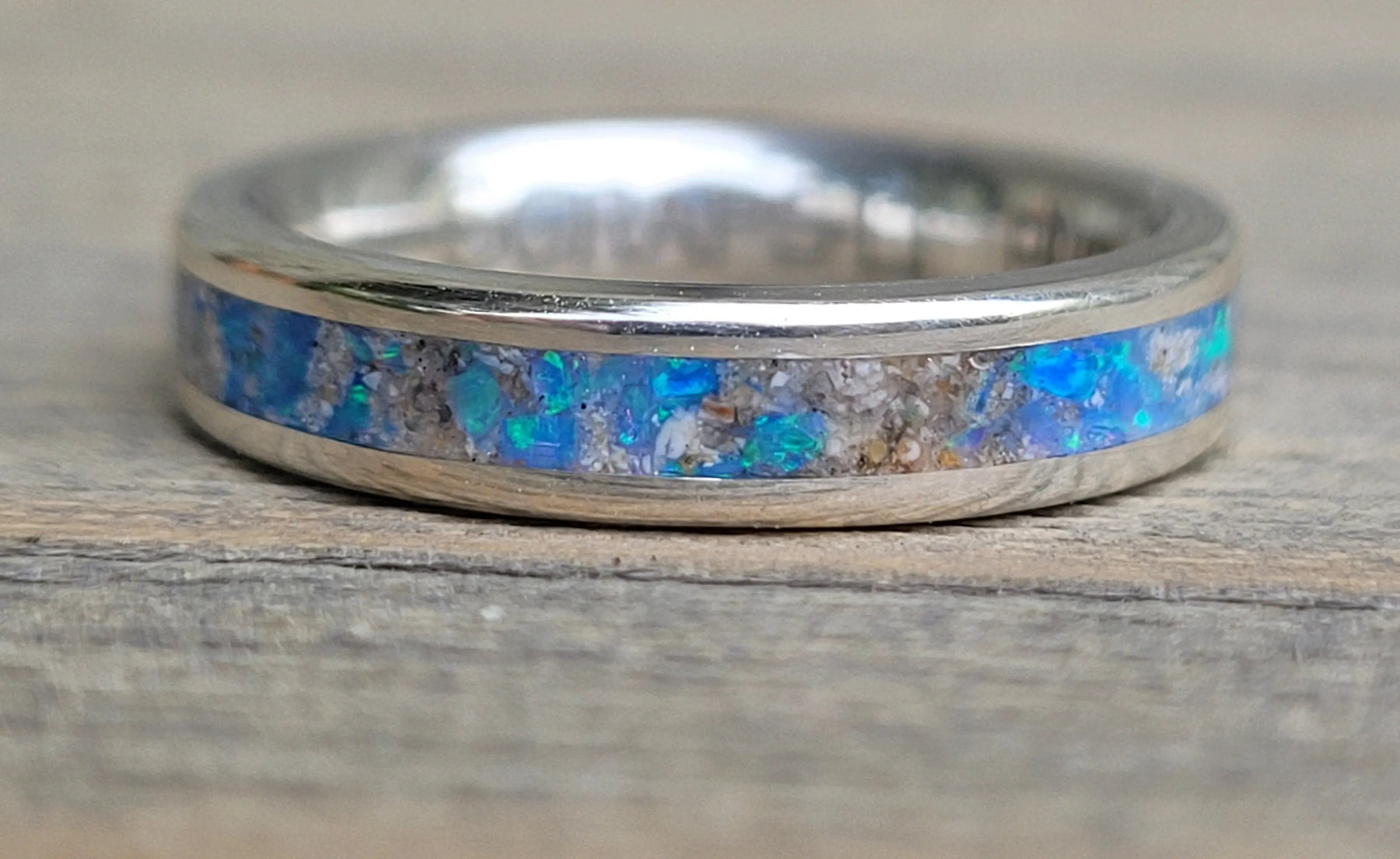 Sterling silver memorial ring with opal and ash inlay, set on a wooden surface.