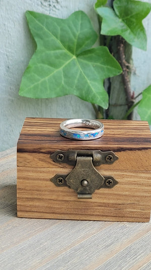 Sterling silver memorial ring with opal and ash inlay on a wooden box.