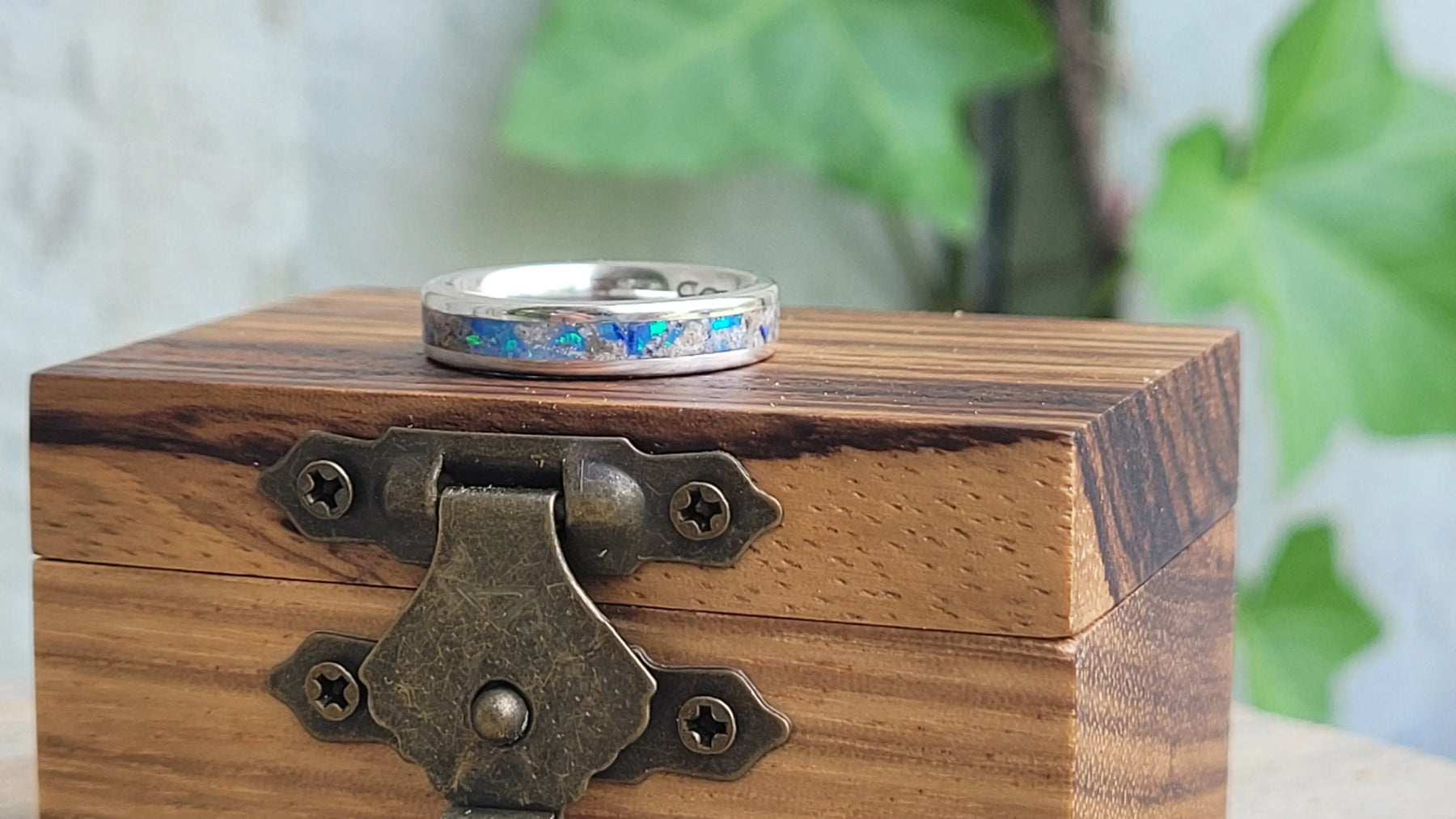 Sterling silver memorial ring with opal and ash inlay on a wooden box.