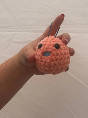 Hand holding handmade orange crochet Stress Blob plush toy with blue chain and facial features for stress relief.