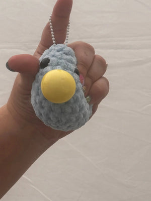 Stress Blob Toy: Hand holding a blue, plushie bird squeeze toy from Main Street Collective with a yellow button beak.