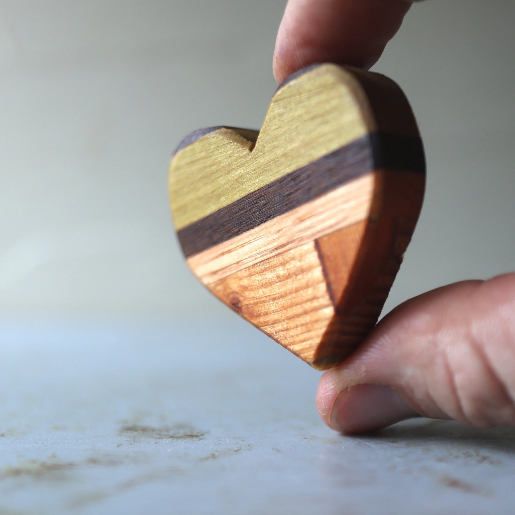 Hand holding a striped wooden heart made from assorted wood pieces.