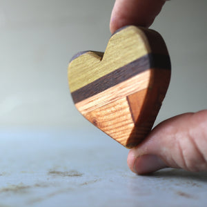 Hand holding a striped wooden heart made from assorted wood pieces.