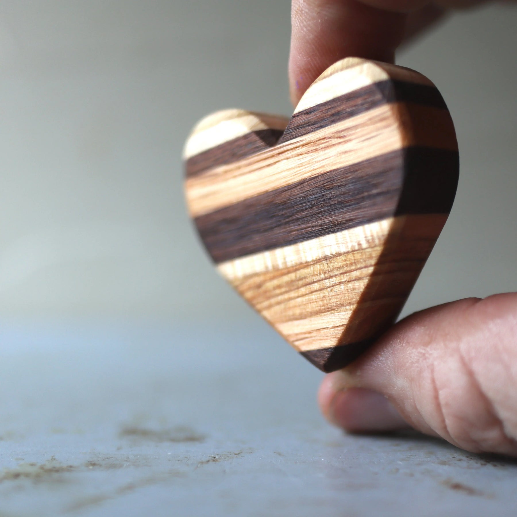 Wooden heart held between fingers with striped wood pattern.