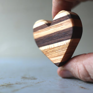 Wooden heart held between fingers with striped wood pattern.
