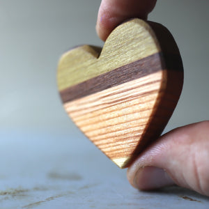 Wooden heart with stripes of different wood held by fingers