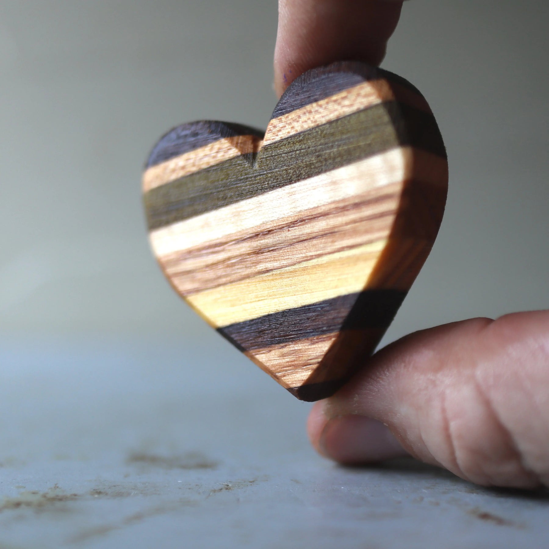 Wooden heart made of colorful striped wood held between fingers.