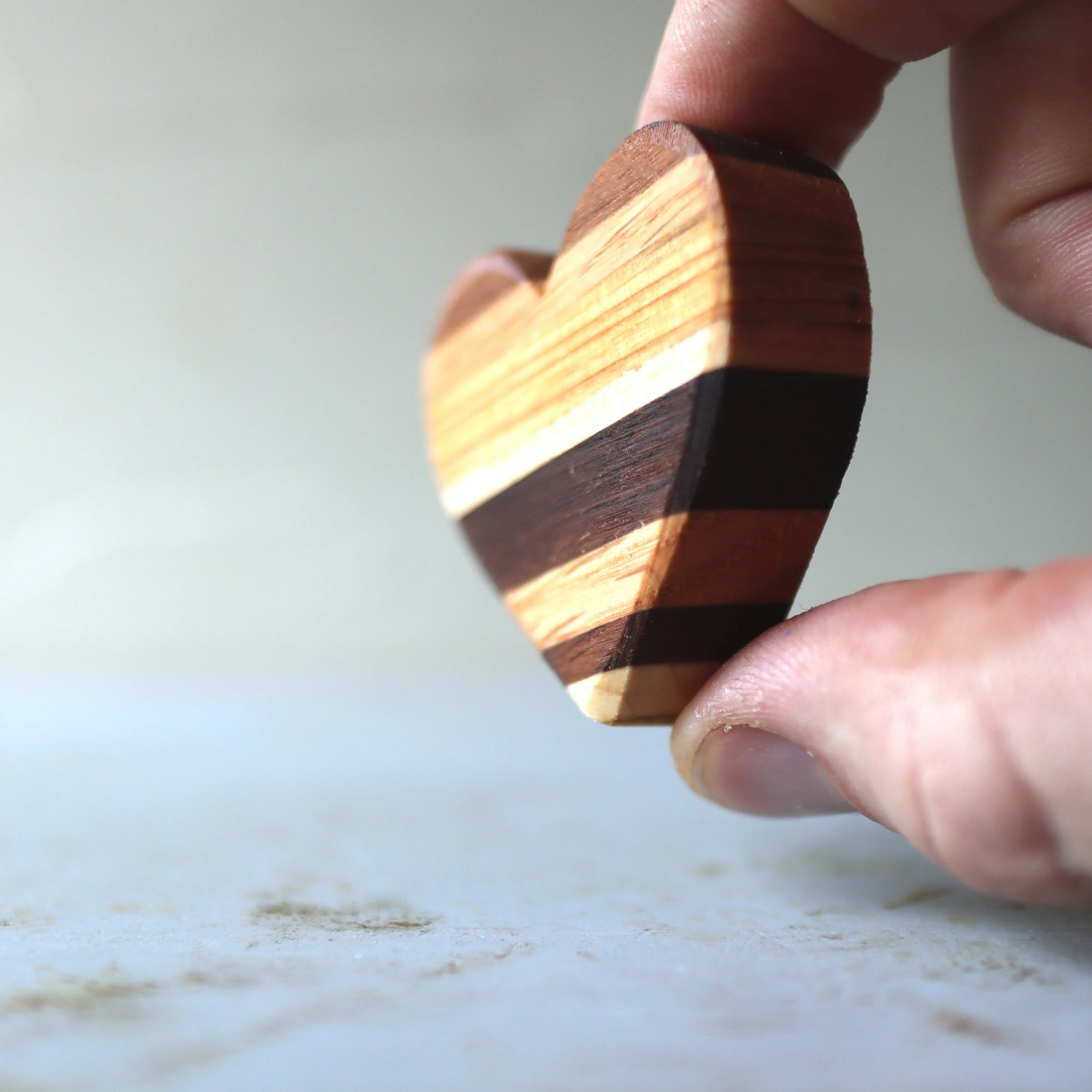 Striped wooden heart made of multi-colored wood segments, held between fingers.