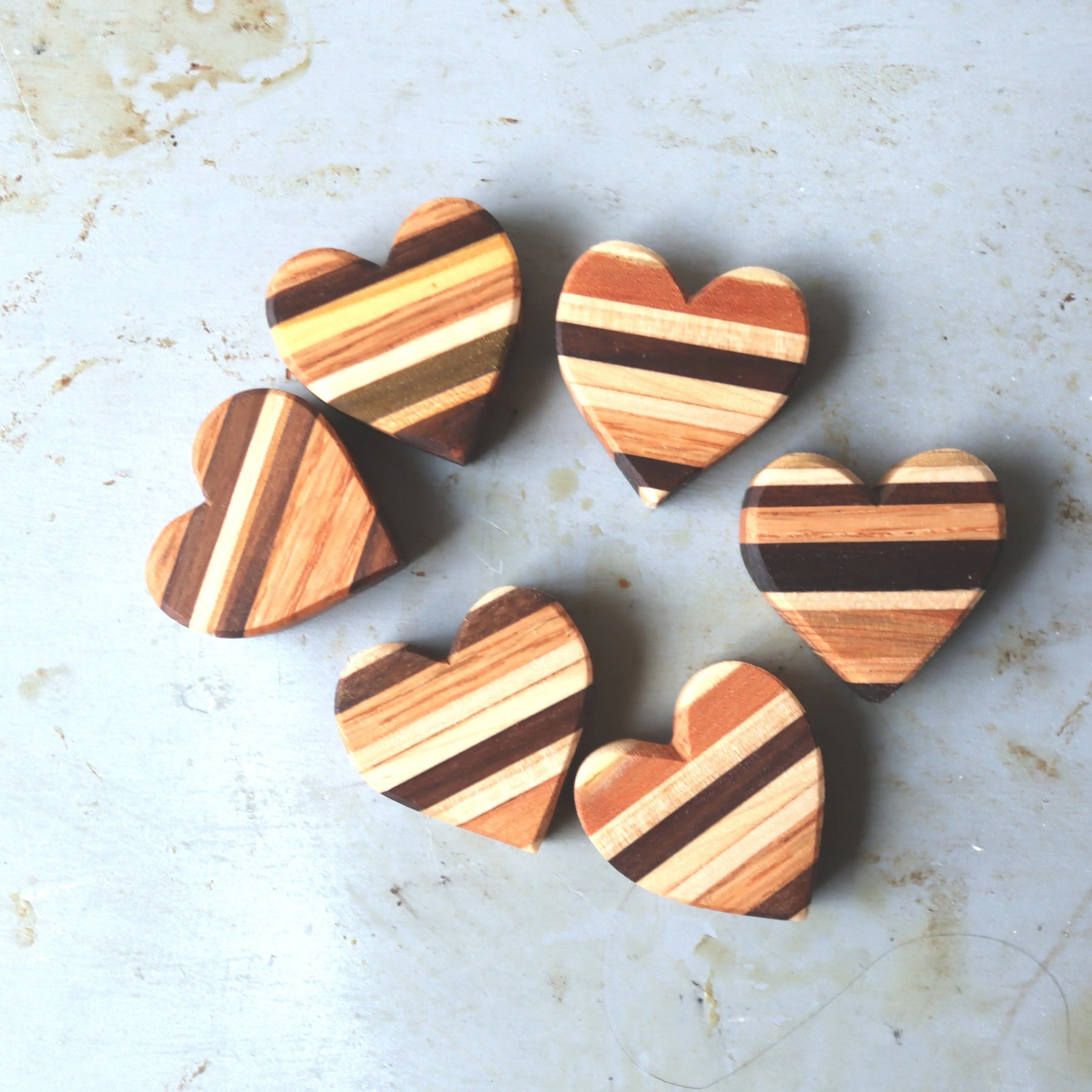 Six striped wooden hearts arranged in a circle on a textured surface.