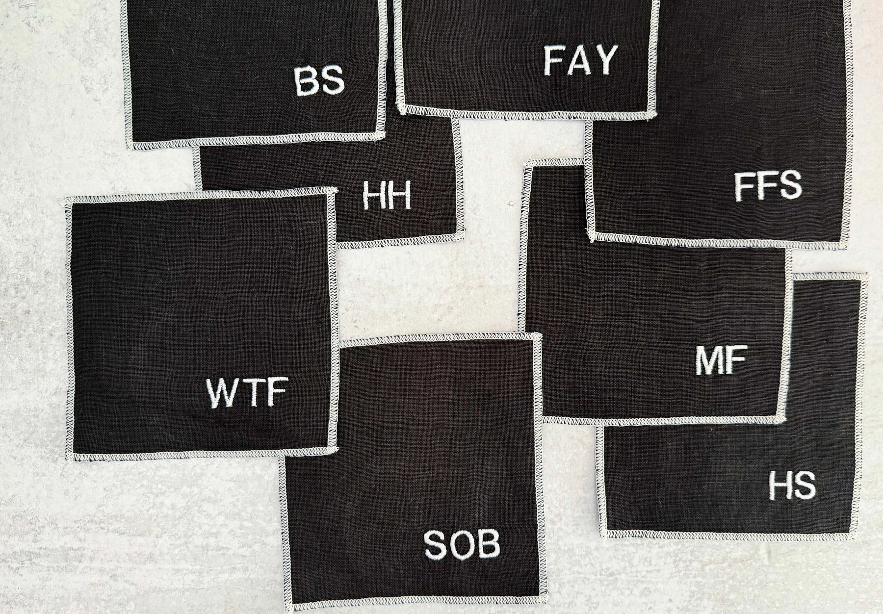 Black linen cocktail coasters with white embroidered letters.