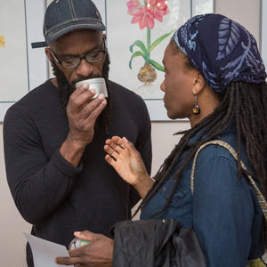 Man smelling a soy wax candle tin while talking to a woman.