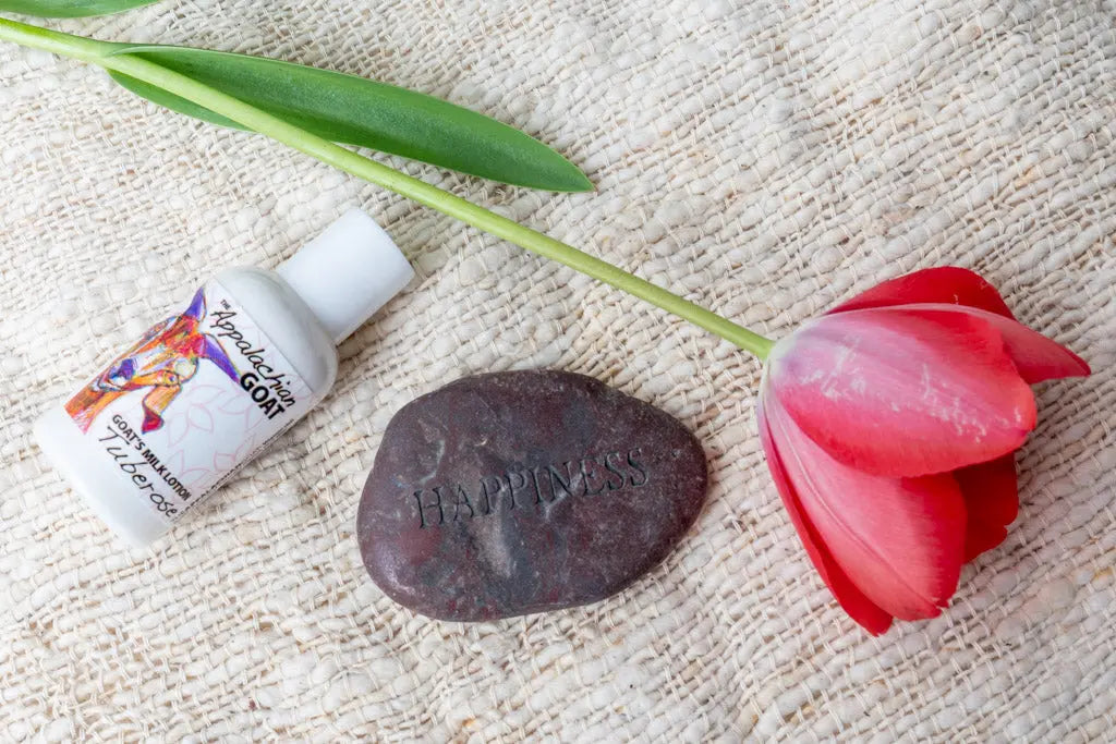 Appalachian Goat Tuberose lotion, red tulip, and 'Happiness' stone on textured fabric.