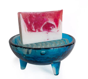 Pink and white marbled goat's milk soap slice in a blue glass soap dish.
