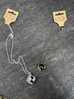 Two dragon claw necklaces on a wood surface. One silver with a clear orb, the other gold with a black orb.