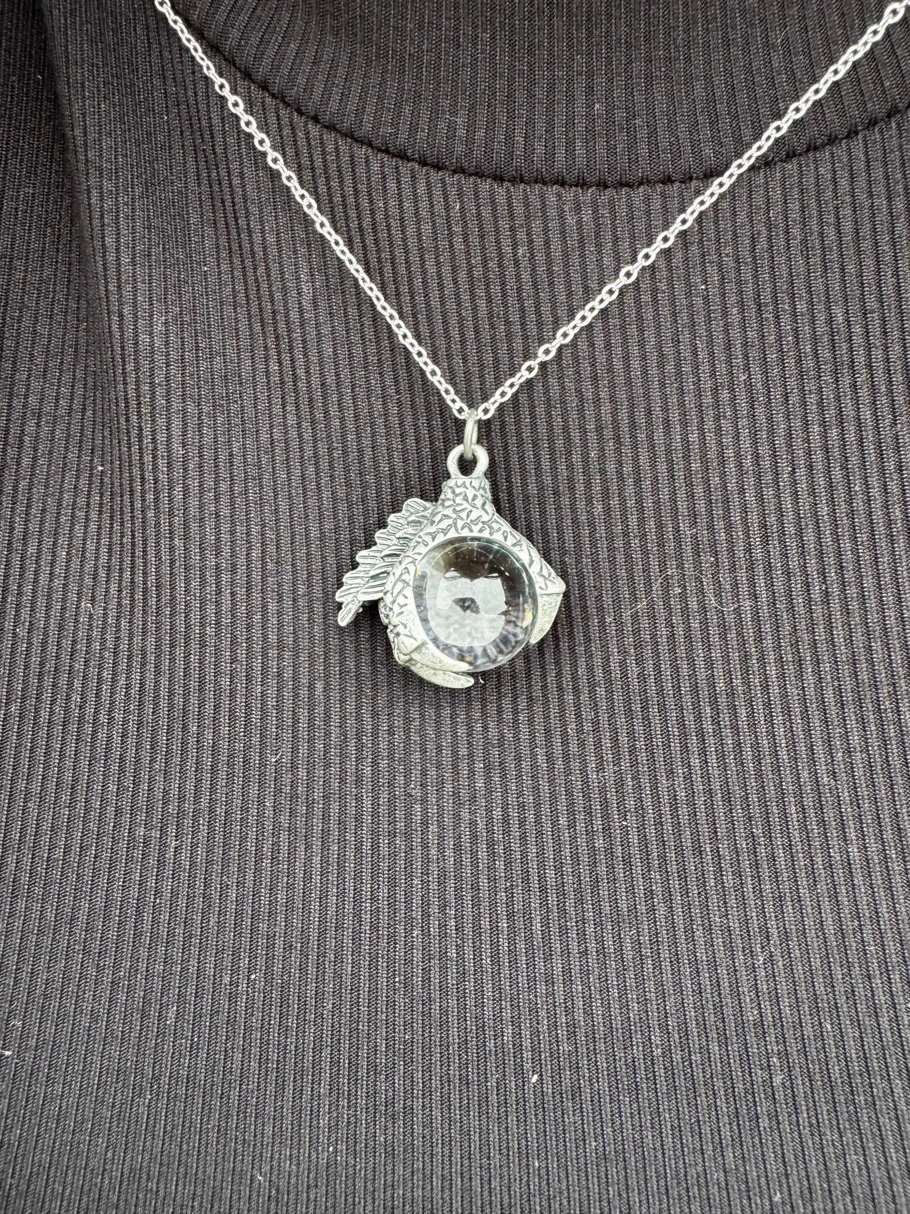 Silver-tone dragon claw necklace with a glass orb pendant on a chain.