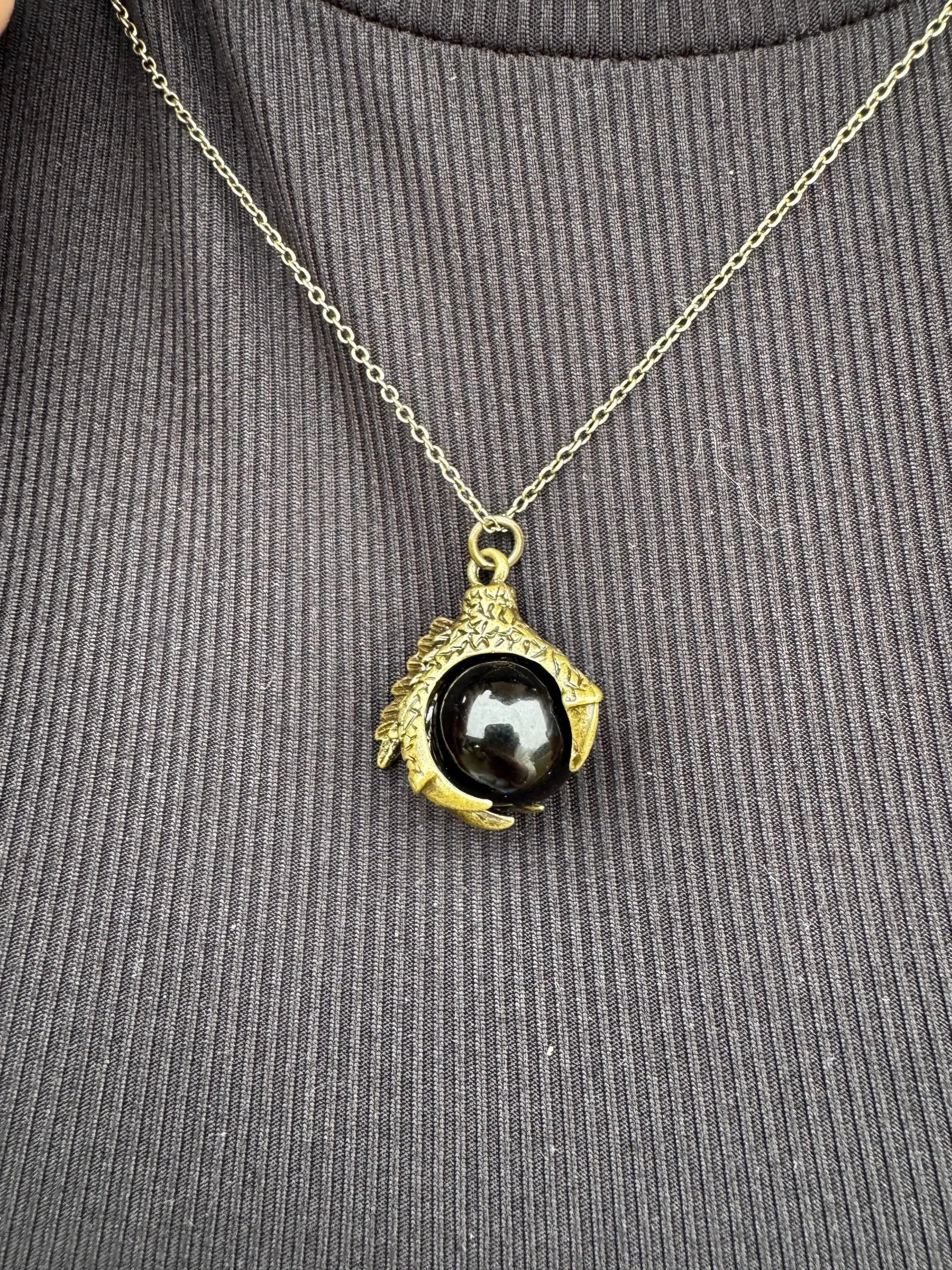 Dragon claw necklace: Gold claw pendant holding a shiny black orb on a silver chain.