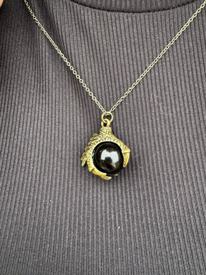 Dragon claw necklace: Gold claw pendant holding a shiny black orb on a silver chain.