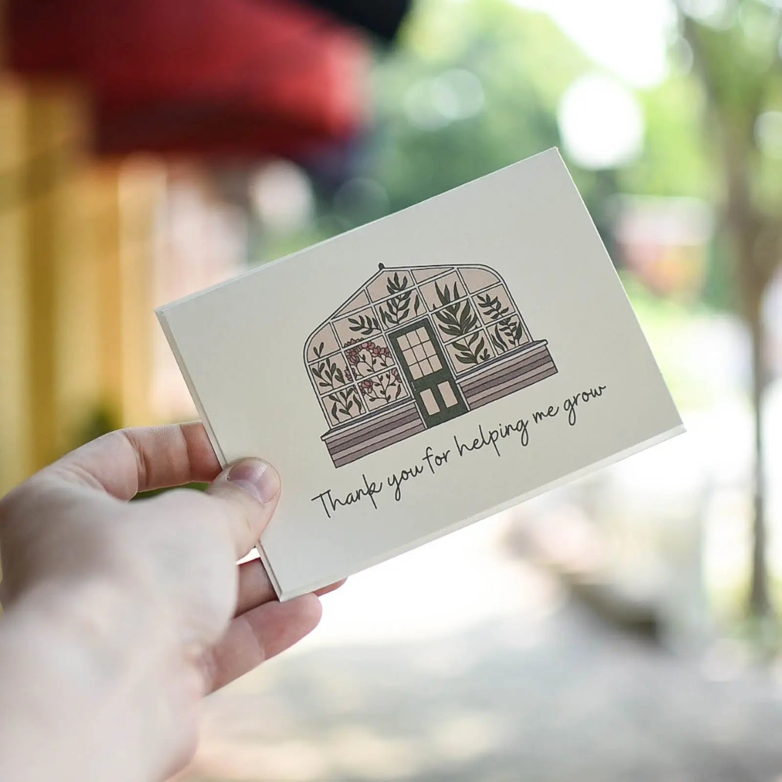 Greeting card with greenhouse illustration and 'Thank you for helping me grow' text held by hand