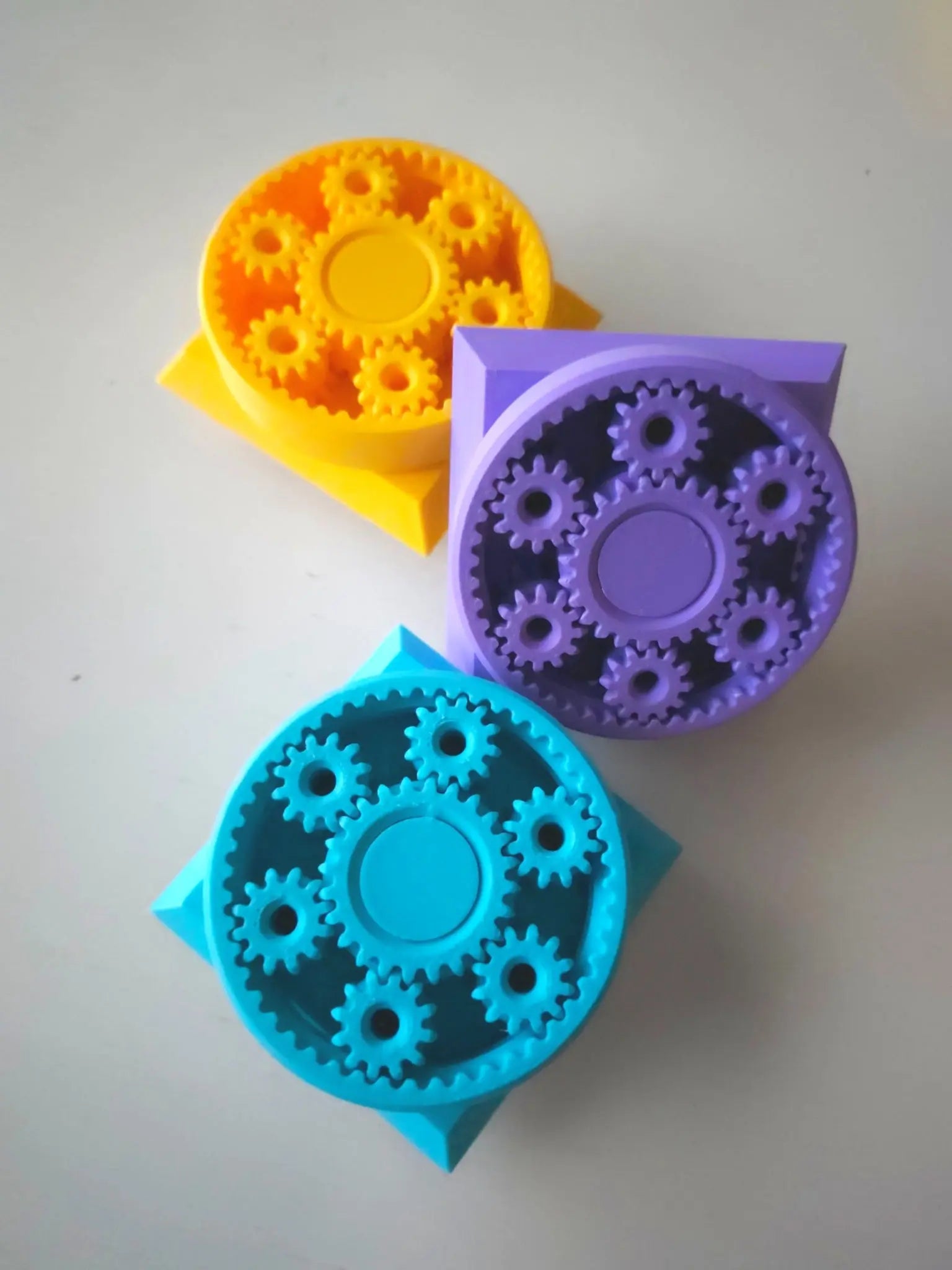 Three colorful gear-shaped fidget cube face on a light gray background
