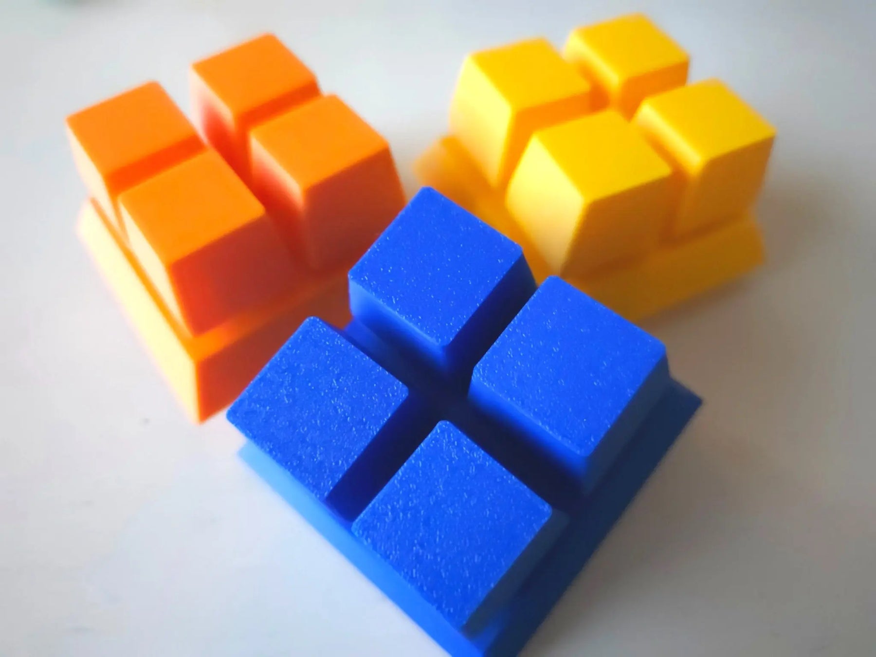 Three colorful fidget clicker blocks in orange, yellow, and blue on a white background