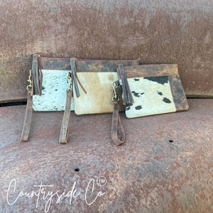 Multiple cowhide leather wristlets with leather trim and fringe on a rusty surface.