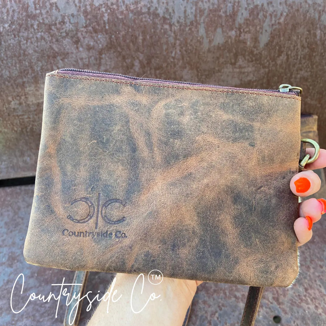 Brown distressed leather wristlet with Countryside Co. logo and orange-tipped fingers.
