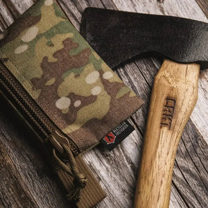 Camouflage tactical pouch next to a CRKT axe with a wooden handle on a wooden surface.