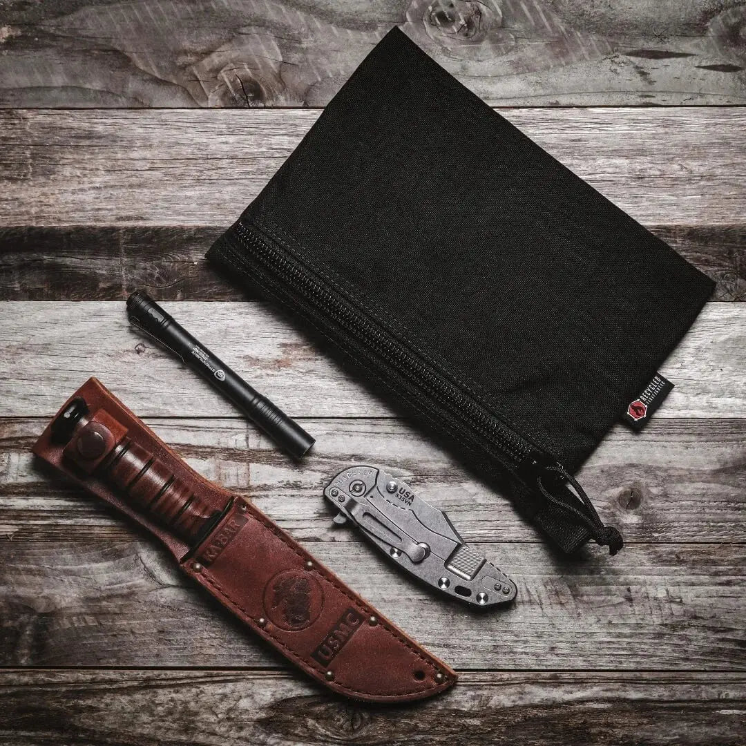 Large black gear pouch with a flashlight, KA-BAR knife, and folding knife on a wooden background.