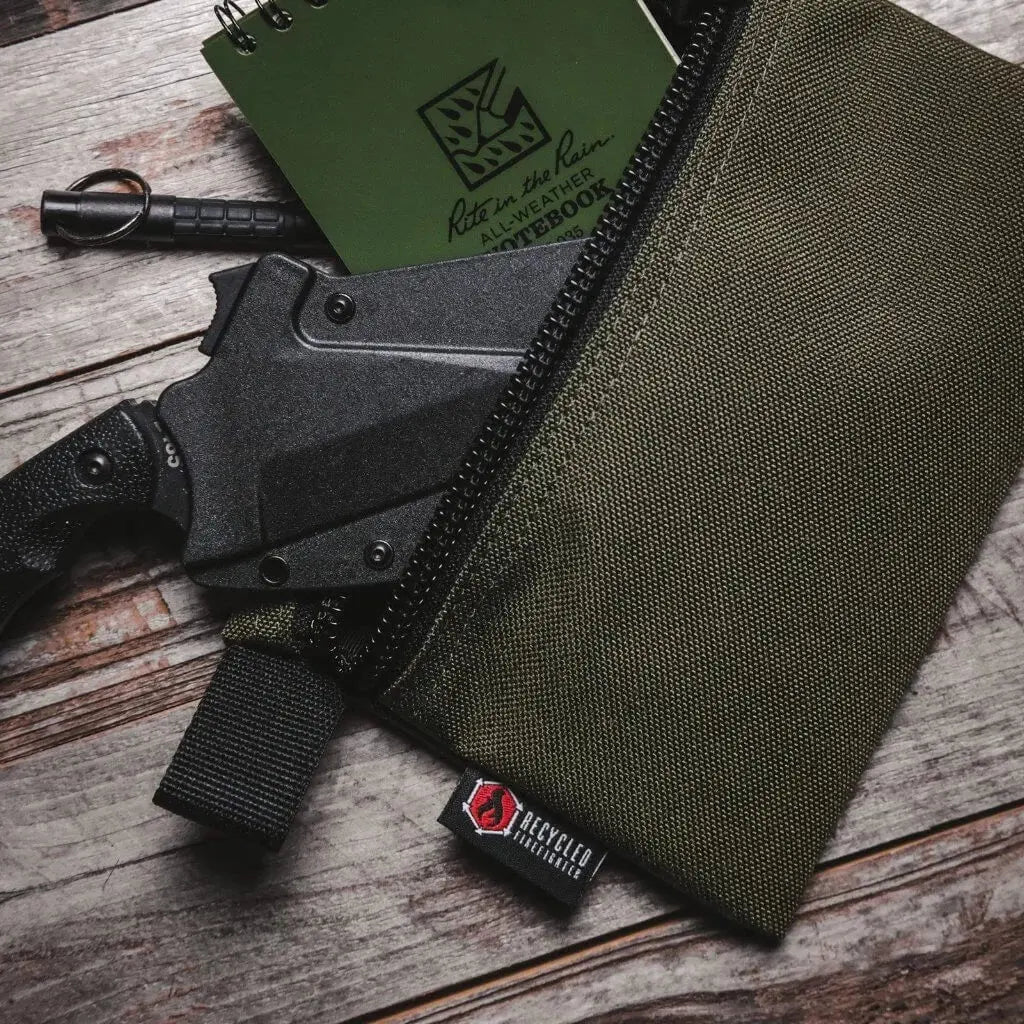Green zippered gear pouch with a notebook and knife on a wooden surface.