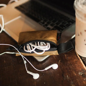 Brown Truckie small pouch with white earbuds spilling out, near a laptop.