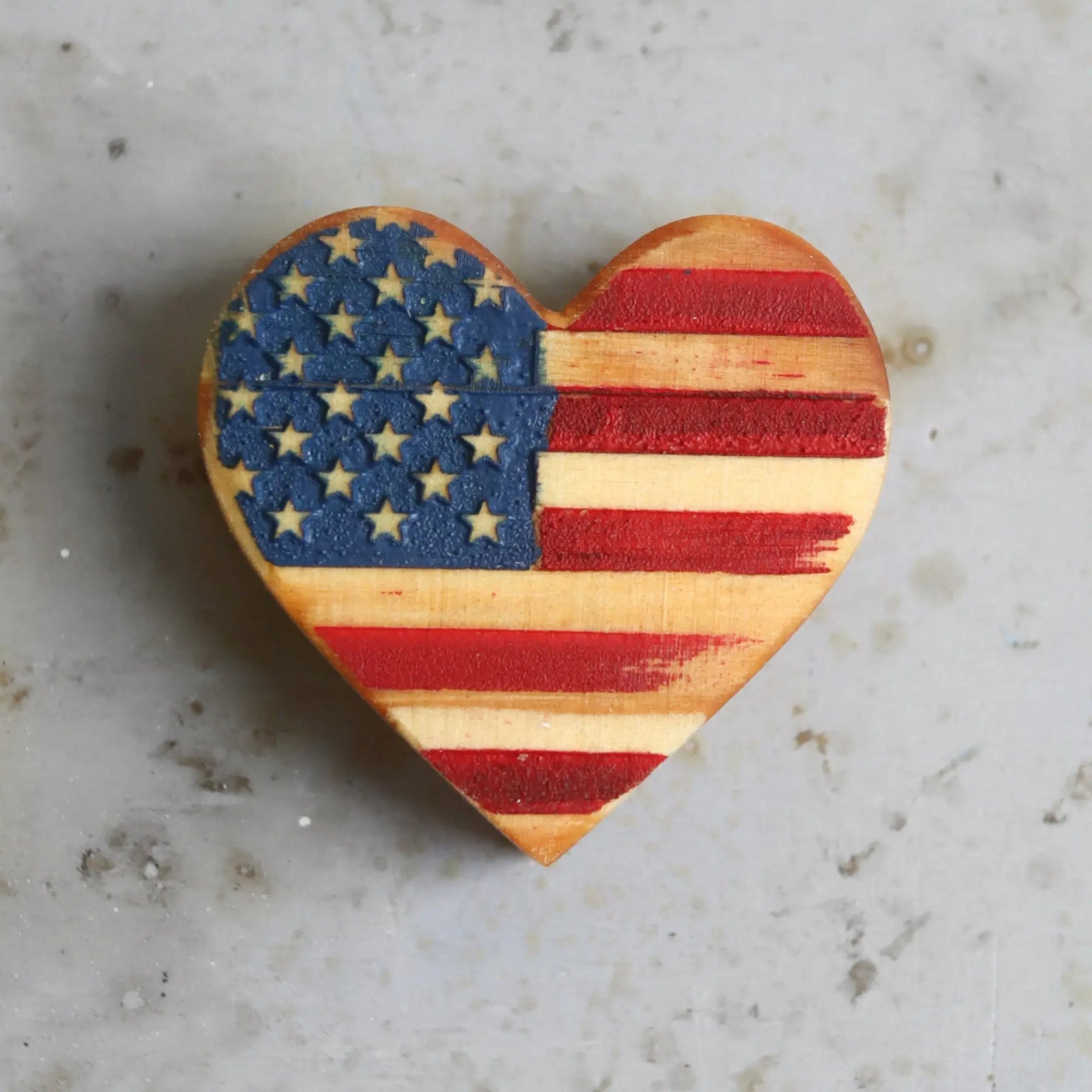 Wooden heart-shaped American flag decoration on a speckled surface.