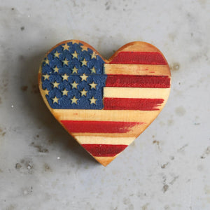 Wooden heart-shaped American flag decoration on a speckled surface.