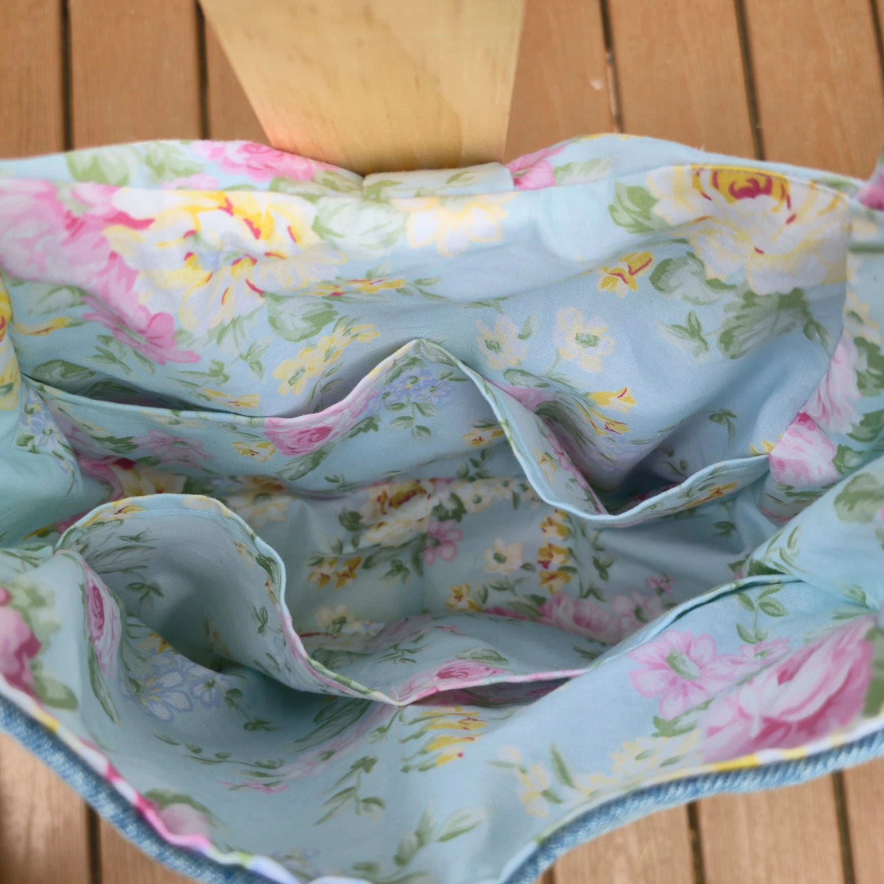 Denim shoulder bag with light blue floral lining and interior pockets.