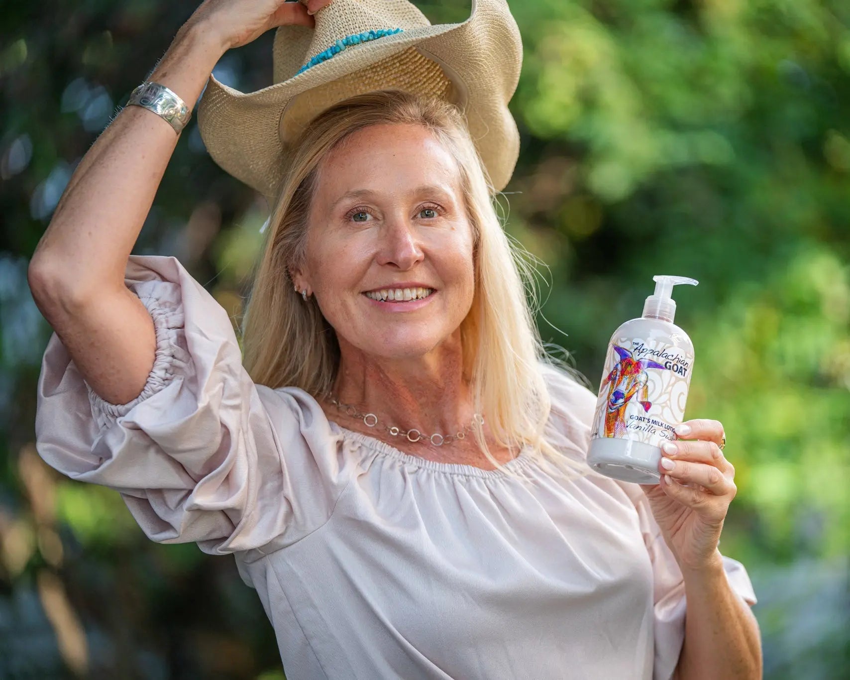 Woman in straw hat holding "The Appalachian Goat" Vanilla Goat's Milk Lotion bottle.