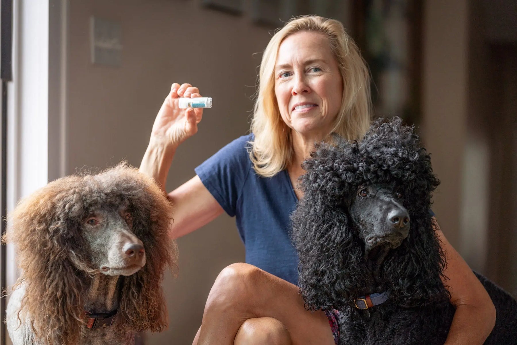 Woman holding a tube of Vanilla Swirl Lip Butter with two poodles.