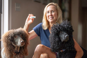 Woman holding a tube of Vanilla Swirl Lip Butter with two poodles.