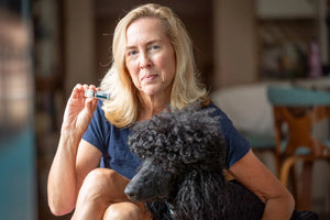 Woman holding a Vanilla Swirl lip balm tube next to a black poodle.
