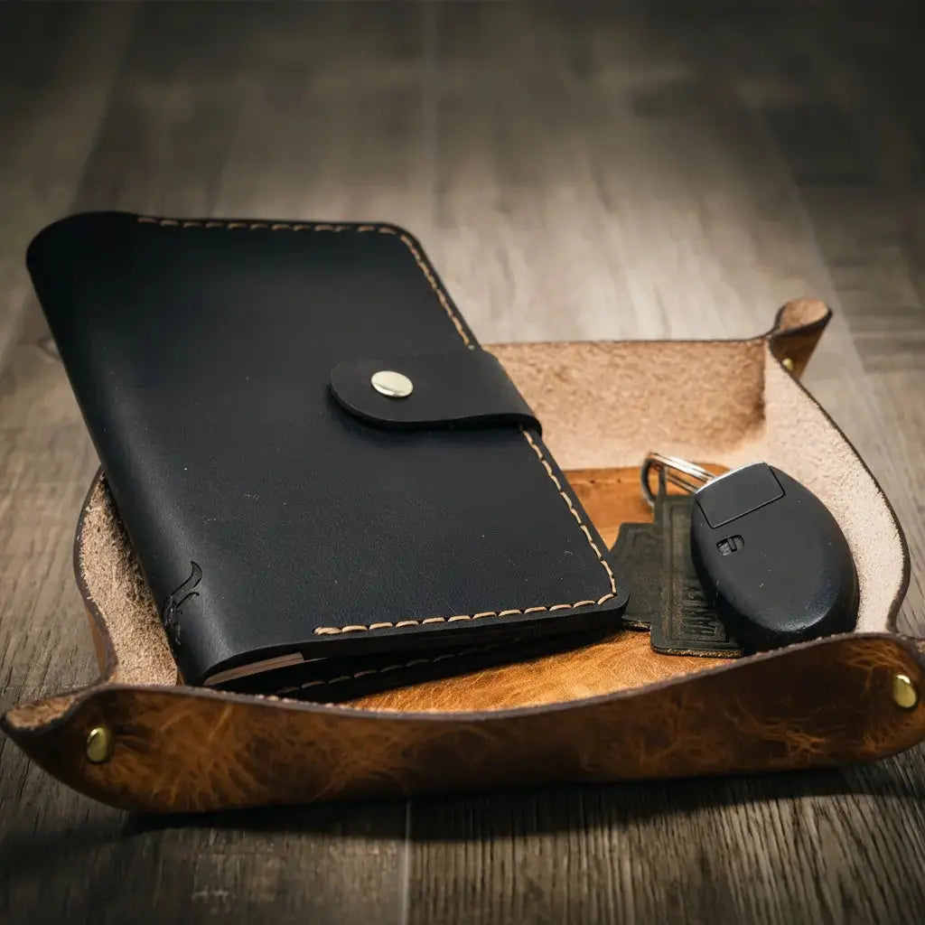 Black leather valet tray with snap closure and car keys in a brown leather catch-all tray