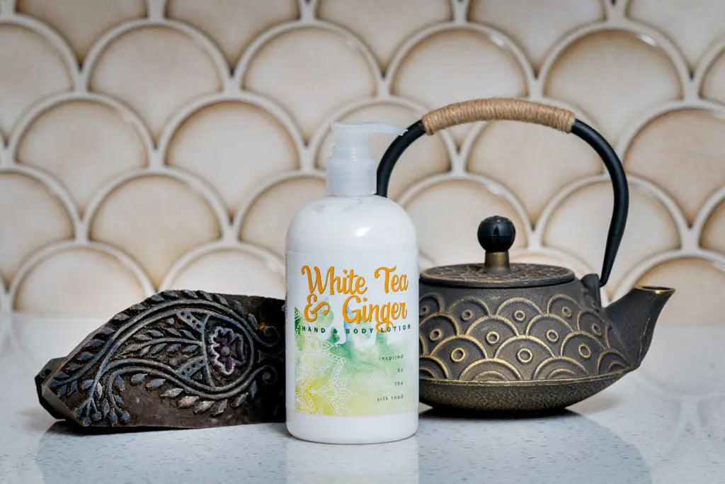 White Tea & Ginger hand lotion bottle next to cast iron teapot and carved block.