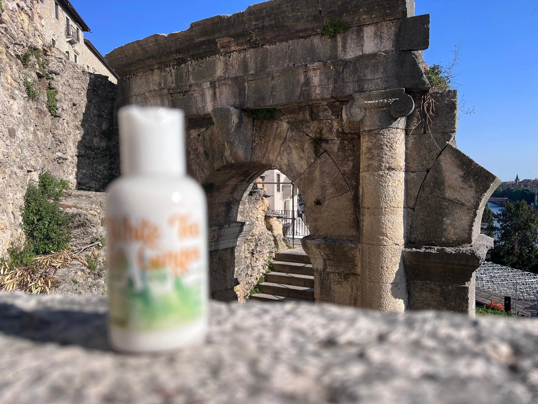 White lotion bottle with green and orange label in front of ancient stone ruins and blue sky.