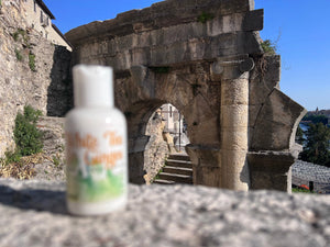 White lotion bottle with green and orange label in front of ancient stone ruins and blue sky.