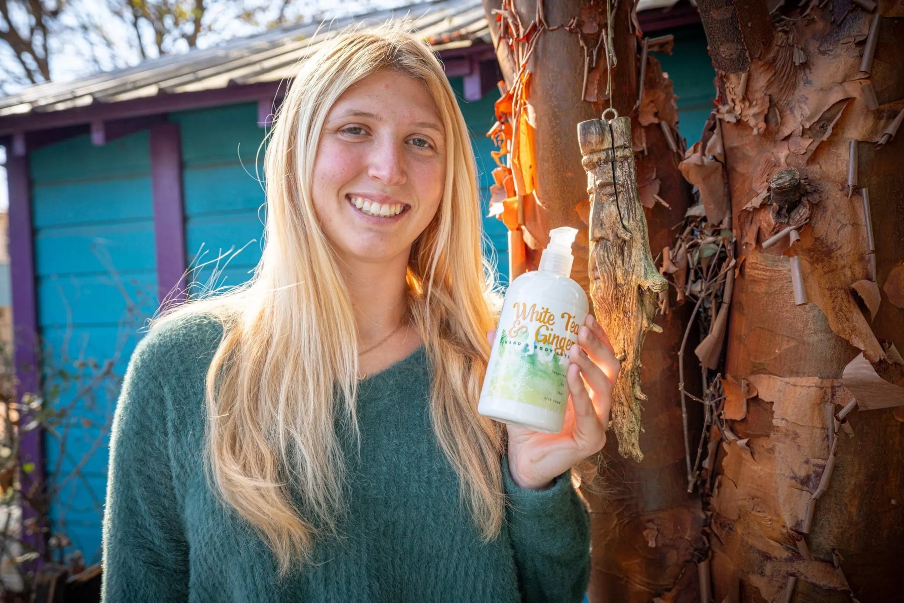 Woman holding Essential Journeys White Tea & Ginger hand and body lotion bottle.