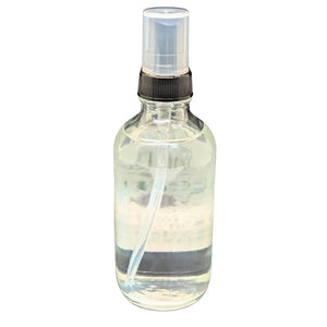 Clear glass spray bottle with black nozzle and cap filled with clear liquid.