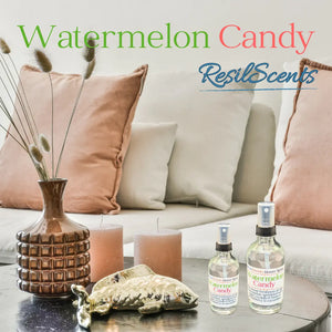 Room scene with ResilScents Watermelon Candy sprays, vase, candles, and decorative fish on a table with pillows.