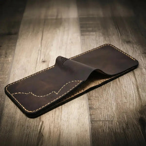 Black hand-stitched leather bifold wallet on a wooden surface.