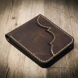 Brown leather bifold wallet with decorative stitching on a wooden surface.