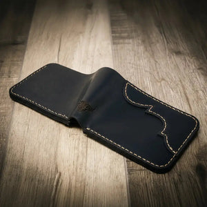 Black leather bifold wallet with white stitching on a wooden surface.