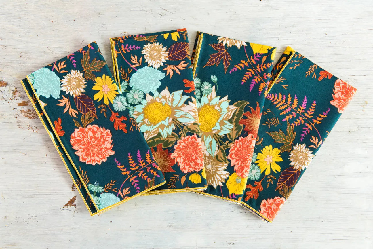 Set of four winter blue floral cloth napkins on a white wooden surface.