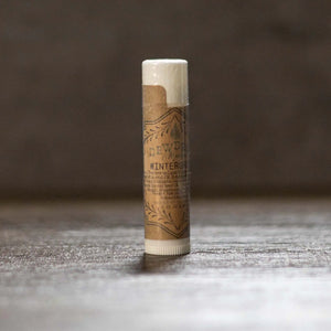Wintergreen lip balm in a clear tube with brown label on a wood surface.