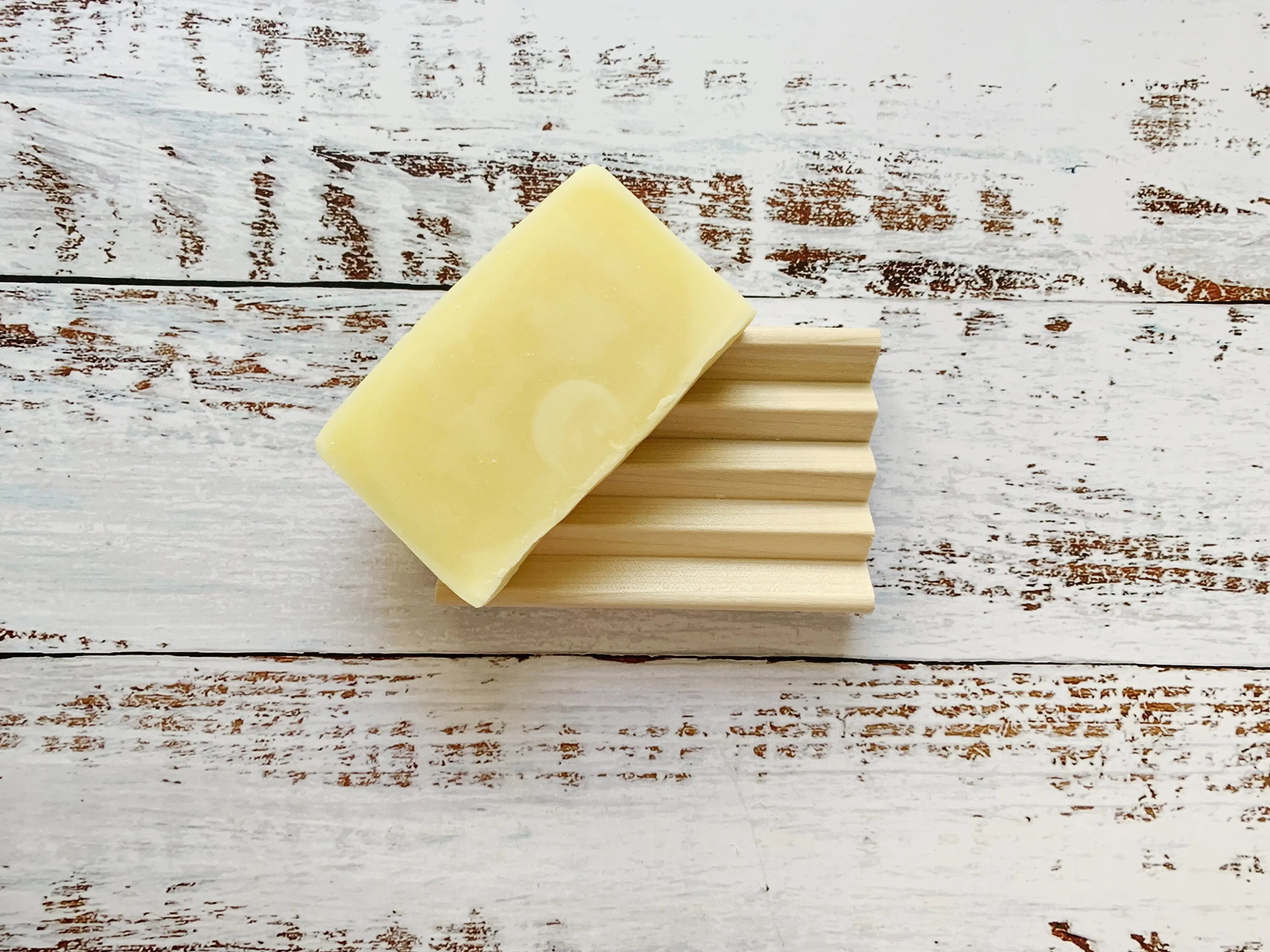Natural wooden soap dish with deep grooves on a distressed white wooden background.